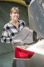 Smiling woman packing luggage into trunk of car