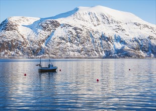 Fishing boat by snow covered mountain in Tromso, Norway
