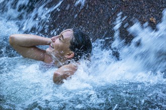 Woman with her eyes closed under waterfall in Phuket, Thailand