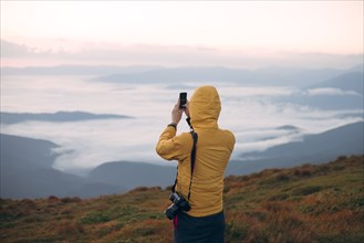 Man in yellow jacket taking photograph on smart phone in the Carpathian Mountain Range
