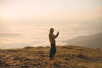 Man in yellow jacket taking photograph on smart phone in the Carpathian Mountain Range