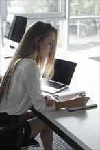Young businesswoman writing notes at desk
