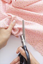 Hands of woman cutting pink floral pattern fabric