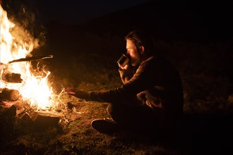Man drinking by campfire