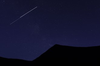 Shooting star above silhouette of mountain