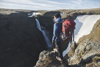 Hiker with backpack on cliff by Haifoss waterfall in Iceland