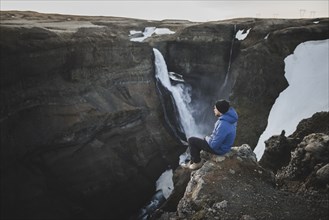 Hiker sitting on cliff by Haifoss waterfall in Iceland