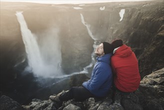 Hiker couple sitting on cliff by Haifoss waterfall in Iceland