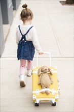 Girl pulling suitcase with teddy bear strapped to it