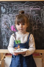Girl holding stick and feather craft by blackboard