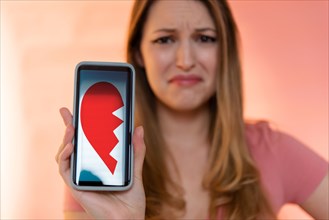 Young woman holding smart phone displaying broken heart