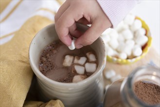 Girl's hand putting marshmallows in hot chocolate