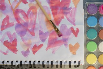 Paintbrush on watercolor painting of hearts by paints