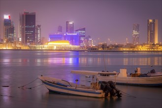Moored motorboats by city skyline at night in Manama, Bahrain