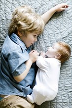 View directly above boy with his baby brother lying on bed
