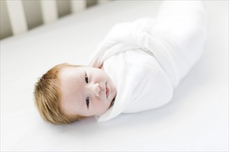Swaddled baby boy in cot