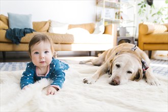 Baby girl and dog lying on rug