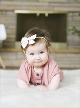 Baby girl wearing bow hair band lying on rug