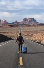Woman walking with suitcase on road through Monument Valley, Utah, USA
