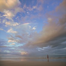 Cloudscape over woman walking on beach in Port Douglas, Australia
