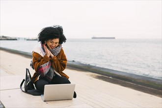 Young woman using laptop on waterfront in Lisbon, Portugal