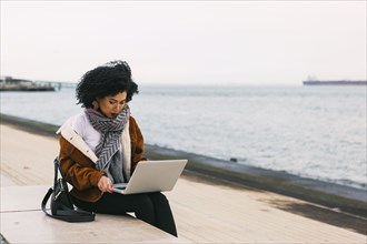 Young woman using laptop on waterfront in Lisbon, Portugal