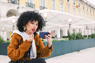 Young woman applying red lipstick using smart phone