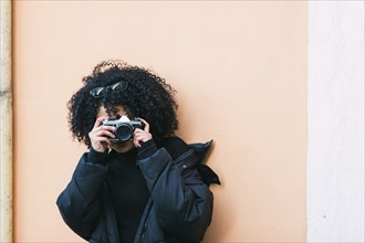 Young woman taking photograph against orange wall