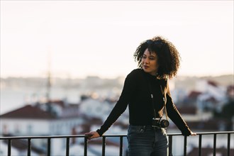 Young woman with camera leaning on railing