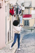 Young woman taking photograph in alley