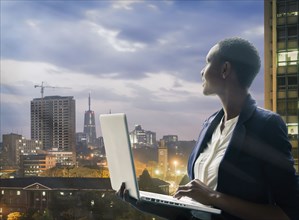 Businesswoman holding laptop by city skyline at sunset in Nairobi, Kenya