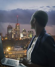 Businesswoman holding laptop by city skyline at sunset in Nairobi, Kenya