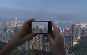 Hands of woman taking photograph with smart phone of cityscape in Hong Kong, China