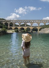 Woman wearing hat standing in Gardon River by Pont du Gard in Vers-Pont-du-Gard, France