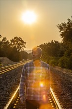 Senior man walking on railroad tracks at sunset