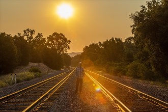 Senior man standing between railroad tracks at sunset