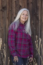 Mature woman wearing checked shirt by wooden wall