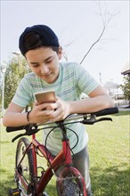 Teenage boy using smart phone leaning on bicycle