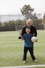 Father with his son holding soccer ball and trophy