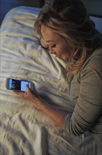 Woman using smart phone while lying on bed