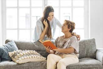 Mother and adult daughter looking at book on sofa