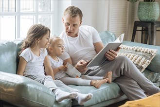 Father reading book to daughters on sofa