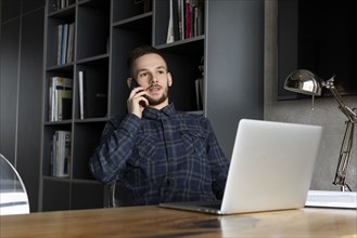 Young businessman on phone by laptop