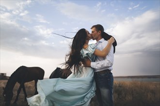 Young couple kissing in field by horses