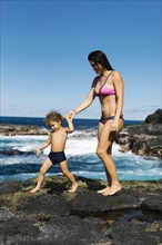 Mother and son walking on rocks by sea