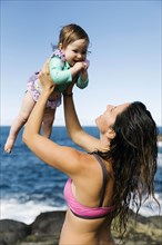 Mother holding her baby girl aloft by sea