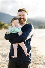 Man holding baby daughter on beach