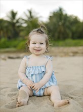 Baby girl wearing blue dress sitting on beach