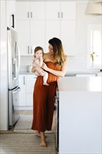 Woman carrying her baby daughter in kitchen