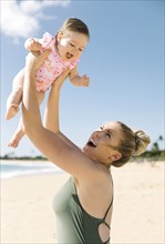 Mother holding her baby girl aloft on beach